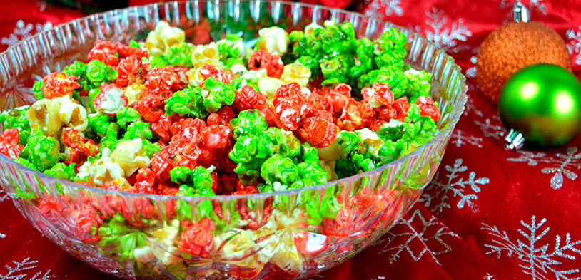 A bowl of christmas popcorn using red, green and white popcorn sitting next to christmas ornaments.