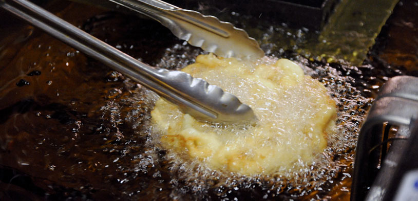 tongs grabbing funnel cake that is cooking in oil.