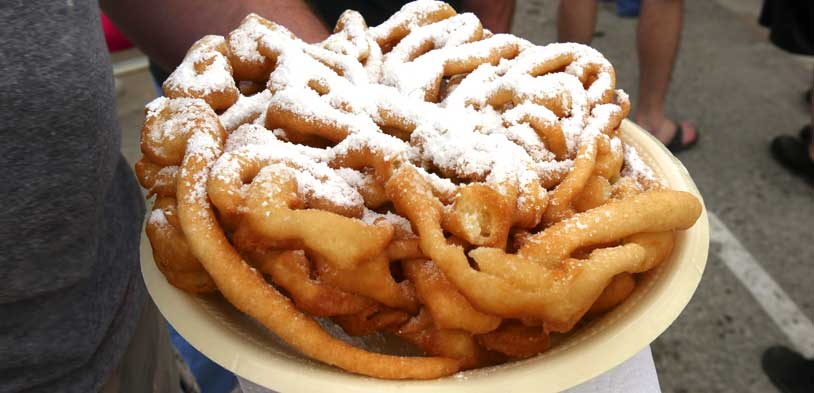 a funnel cake with powder sugar held by a man in a street fair