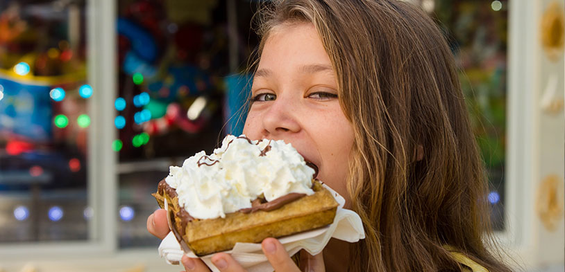 Girl eating a waffle topped with whipped cream and chocolate.