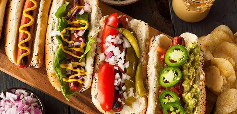 Four gourmet hotdogs sitting on a wood platter.
