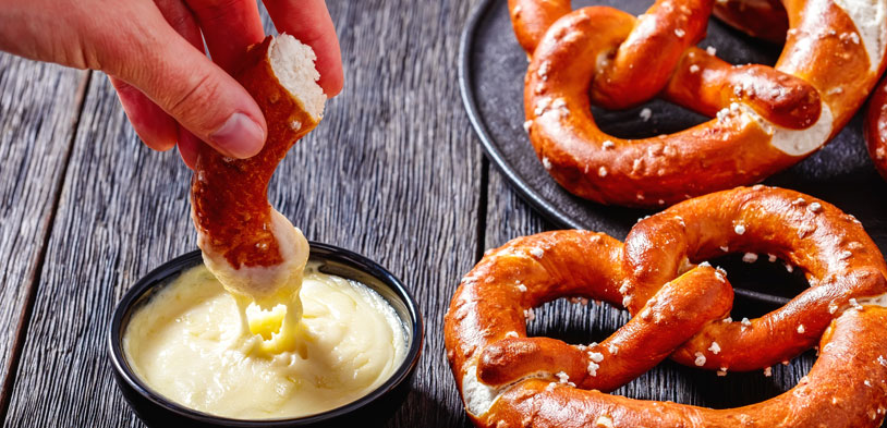 A soft pretzel being dipped into warm cheese dip