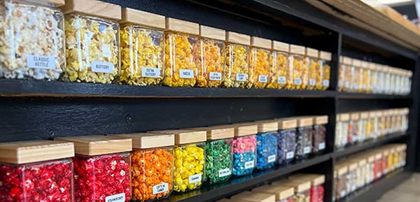 Variety gourmet popcorn from Cole Market line the wall on black shelves