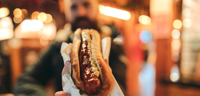 man holds hot dog but background is blurred