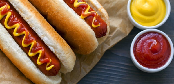 two hot dogs on table with ketchup and mustard on the side