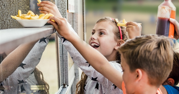 Smiling children at a 幸运168飞艇开奖直播号码查询 Concession stand reaching for a plate of French fries during a youth sports event.