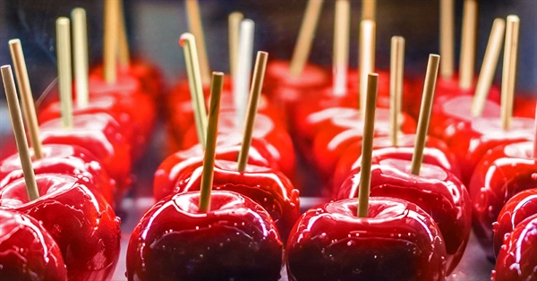 A tray of bright red candy-coated apples with wooden sticks on display.