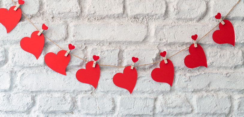 red paper hearts cut out and hung on string against a while brick wall