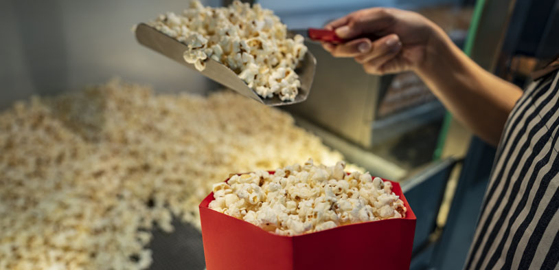 employee at popcorn machine scooping popcorn out and into a popcorn bucket