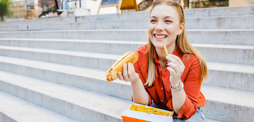 A woman outside enjoys a chili dog and french fries