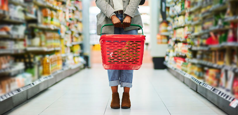 person in grocery aisle holding shopping basket