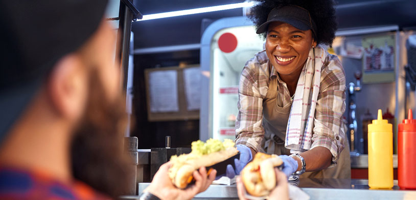 afro american woman holding food as she hands it to customer in food truck