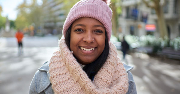 A woman stands in the park in cold weather wearing warm clothes.