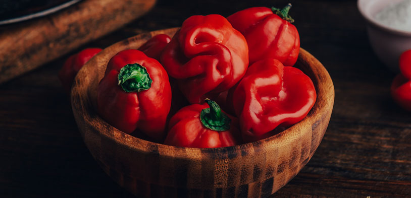 A bowl full of red habanero peppers with green stems