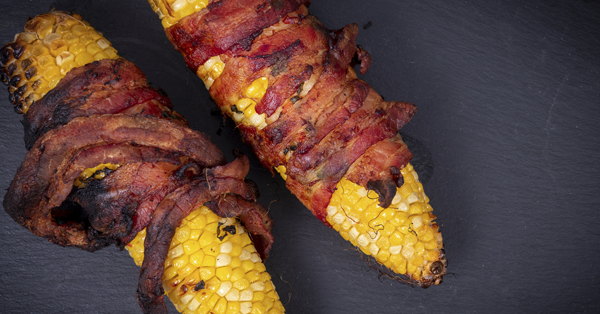 Corn on the cob wrapped with fried bacon strips.
