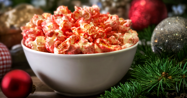 Candy Cane flavored popcorn in a white bowl with Christmas decorations around it.