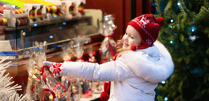 girl with winter coat and hat picking out a gift basket with Christmas tree in background