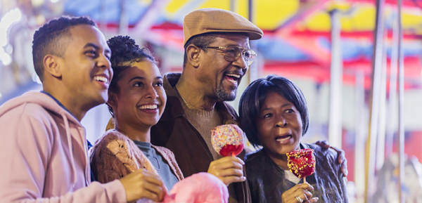 Smiling family enjoying candied apples and cotton candy at an outdoor fair with colorful tents in the background. Smiling family enjoying candied apples and cotton candy at an outdoor fair with colorful tents in the background.