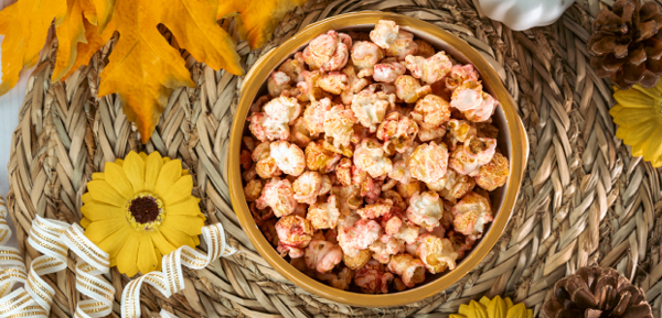 Bowl of fall-flavored popcorn surrounded by autumn leaves, pinecones, and decorative flowers on a woven placemat.