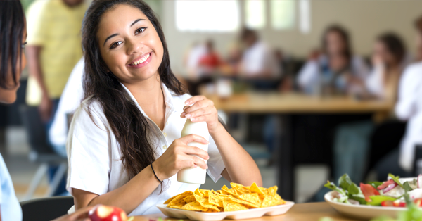 Asian woman sits at lunch table with friend smiling as she is about to enjoy her plate of nachos