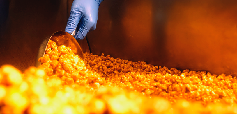 a persons hand wearing a blue glove scoops gourmet popcorn out of a warmer