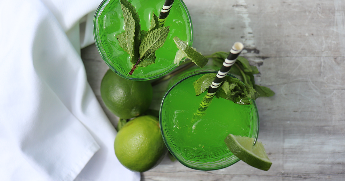 green mojito mocktail with paper straws garnished with fresh mint leaves and lime on a white cloth