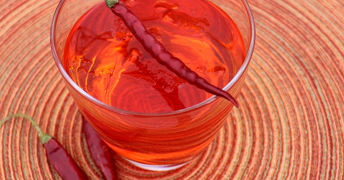 orange-red spicy mango mocktail in glass garnished with spicy red pepper on a orange and beige placemat