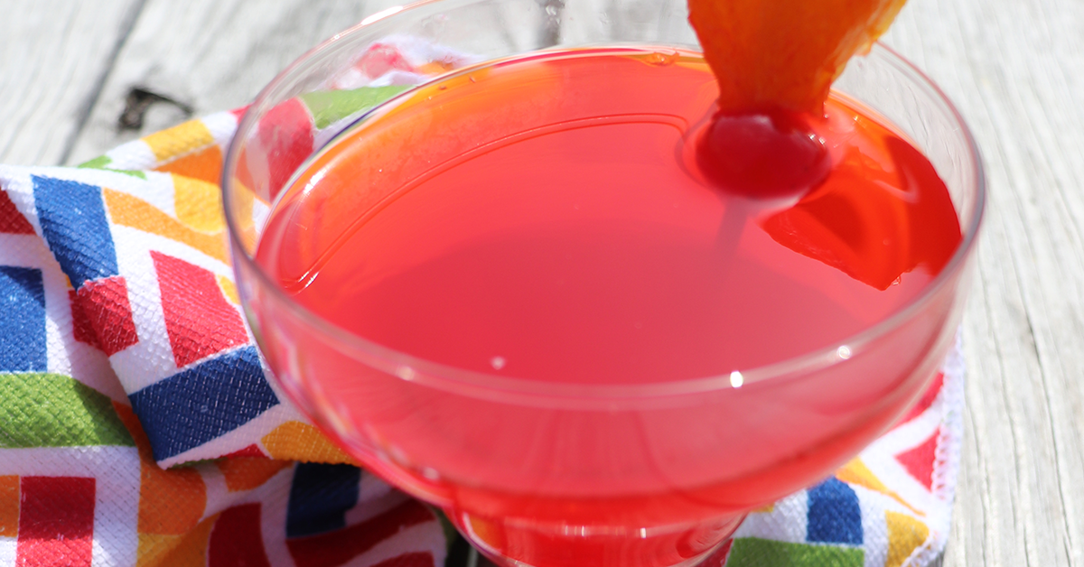 "tequila" sunrise mocktail in cocktail glass garnished with an orange and cherry on colorful patterned cloth