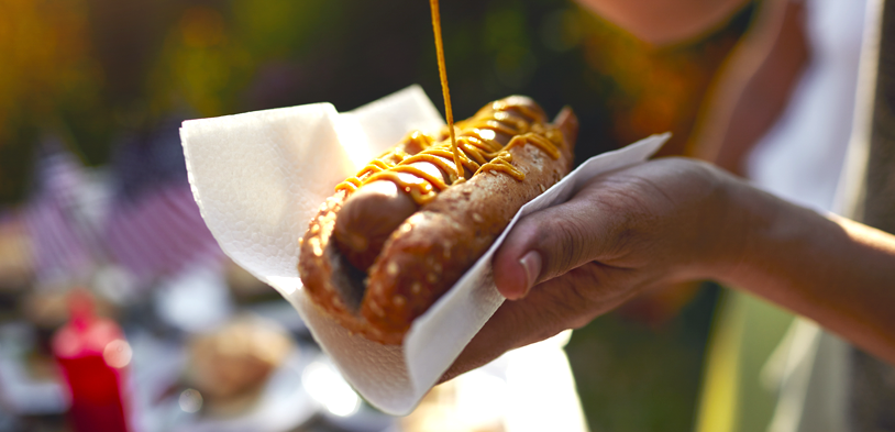 man holds hot dog and pours mustard on it