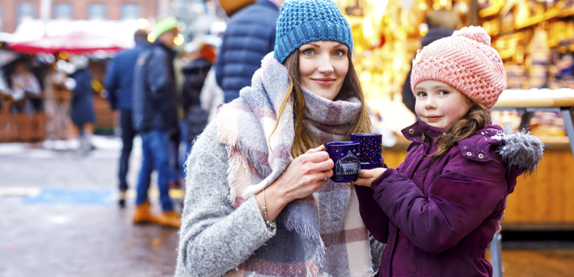 a woman kneels by her daughter outside as they share a warm drink