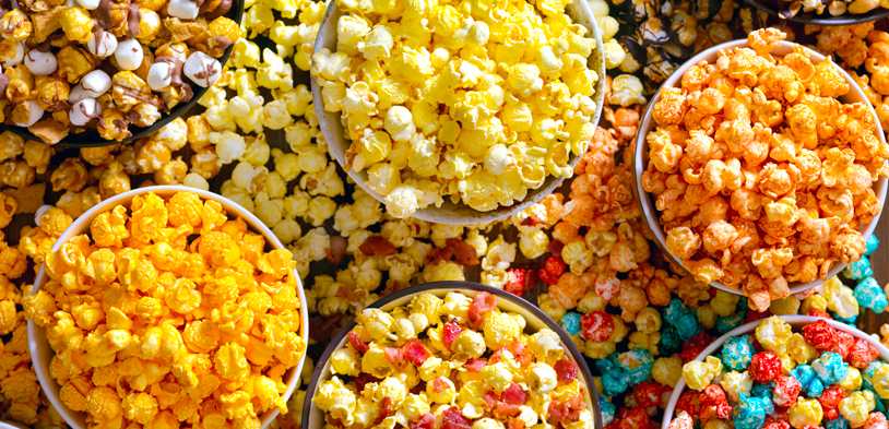 several bowls on a table filled with several varities of gourmet popcorn and candies