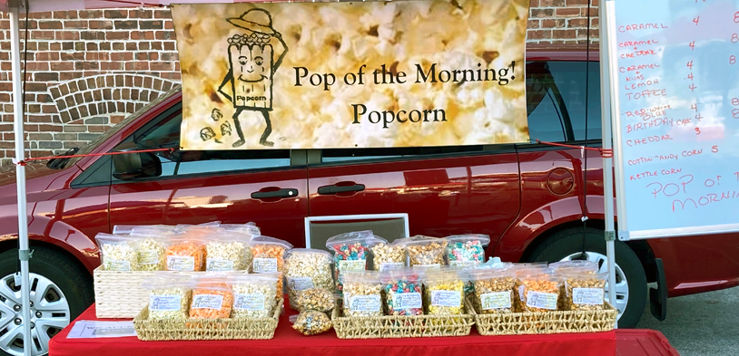 multiple types of flavor of popcorn sit in front of a van and the business sign