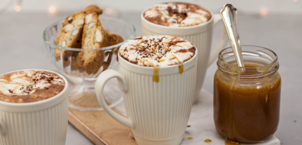 Three mugs of salted caramel hot chocolate topped with whipped cream, surrounded by caramel sauce and biscotti. Three mugs of salted caramel hot chocolate topped with whipped cream, surrounded by caramel sauce and biscotti.