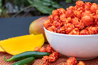 White bowl holding spicy mango flavored popcorn next to a wedge of mango and jalapeno pepper